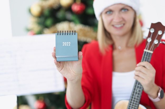 Woman musician holding new year calendar for 2022 near Christmas tree closeup