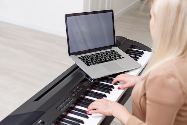 Musicista donna che suona il pianoforte digitale classico a casa durante la lezione online a casa, distanza sociale durante la quarantena, autoisolamento, concetto di educazione online