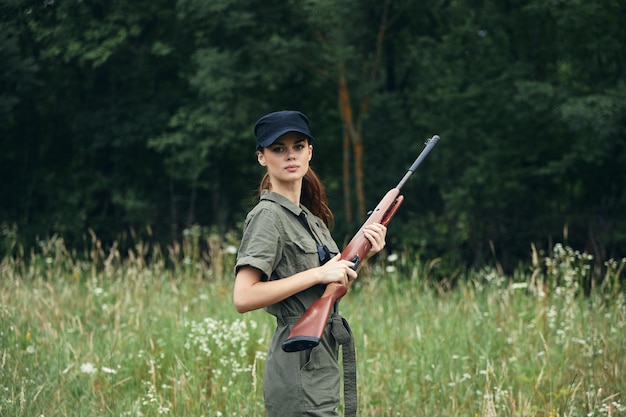 Женщина на природе С оружием в руках черная кепка - образ жизни зеленый комбинезон лесной фон