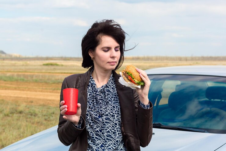 ガラスを手に持った自然の女性がハンバーガーを食べようとしています。