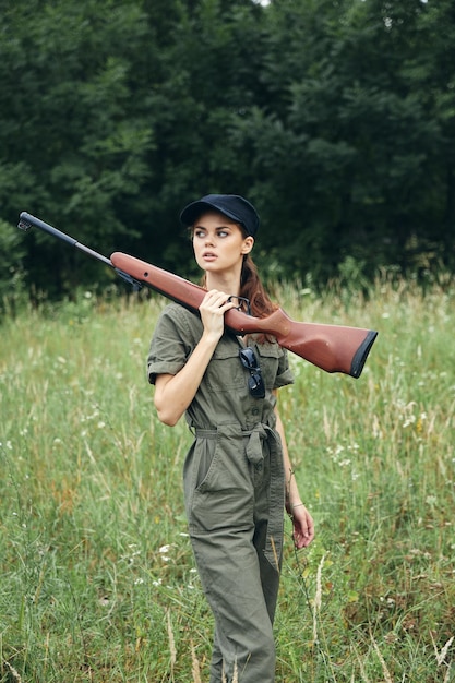 Woman on nature with a gun in his hands looking to the side green overalls fresh air