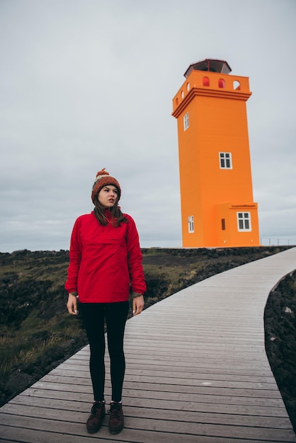 아이슬란드의 큰 주황색 등대 근처에 있는 여자. 패션과 자연 개념의 예술적 파노라마.