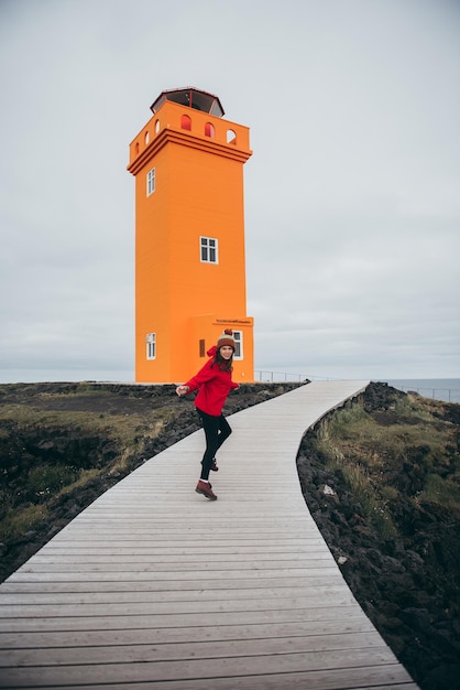 Woman near big orange lighthouse in iceland.fashion and nature
concept artistic panorama.