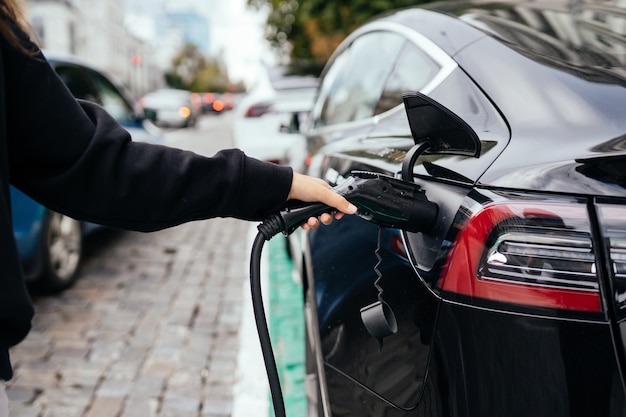 電気自動車の近くの女性。充電ステーションで充電された車両。