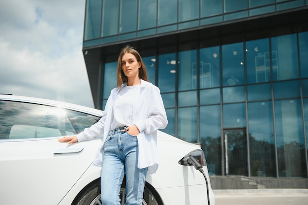 Donna vicino all'auto elettrica veicolo caricato presso la stazione di ricarica