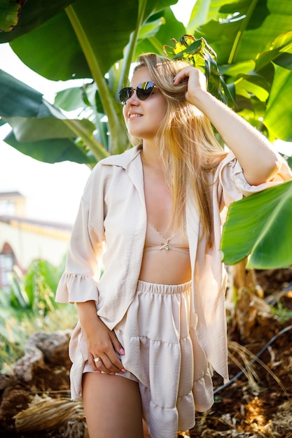 Woman near a large green leaf of a banana tree in nature in the park. Tropical plants and attractive girl walking