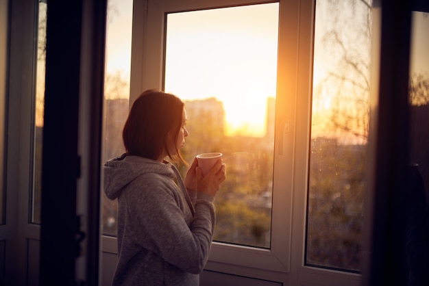 Woman near window at sunset in isolation at home for virus outbreak. Stay home concept