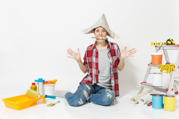 Woman in newspaper hat sitting on floor with brush in mouth, instruments for renovation apartment isolated on white background. Wallpaper, accessories for gluing, painting tools. Repair home concept.