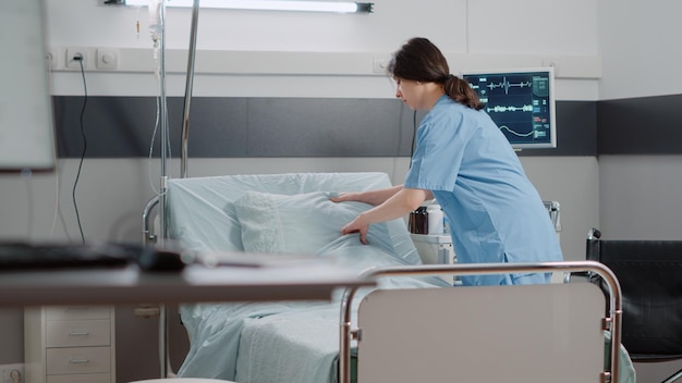 woman nurse making bed in hospital ward for healthcare treatment and recovery. medical assistant preparing reanimation room with oxygen tube and heart rate monitor for patient.