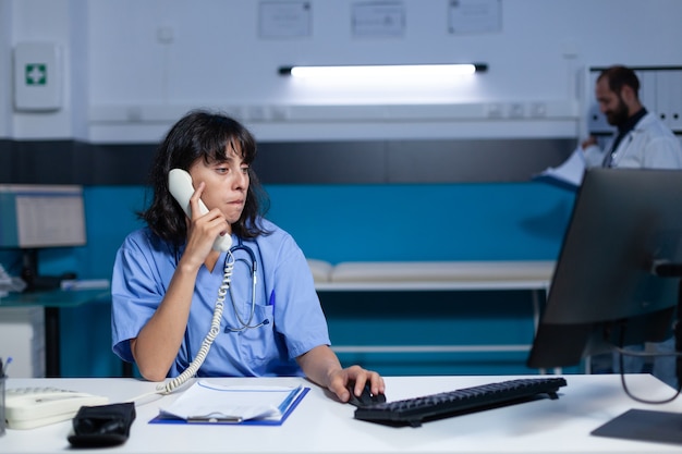 Infermiera in uniforme che usa il telefono fisso per conversare