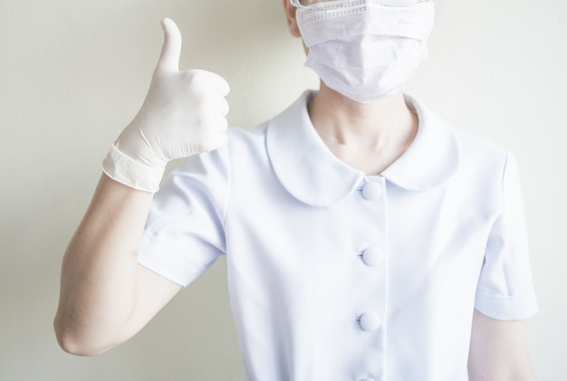 Woman nurse wearing mask raises the thumbs up to compliment people who work at home and social distancing strictly, prevent spreading of coronavirus outbreak.