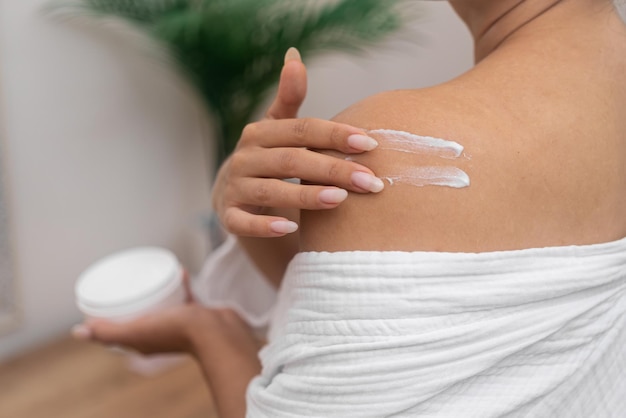 Woman nurtures her shoulder with moisturizing cream turning her home into a haven of body care