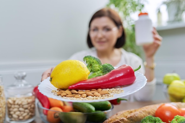 Woman nutritionist pointing at the camera a plate with a set of healthy food and a jar of food additives