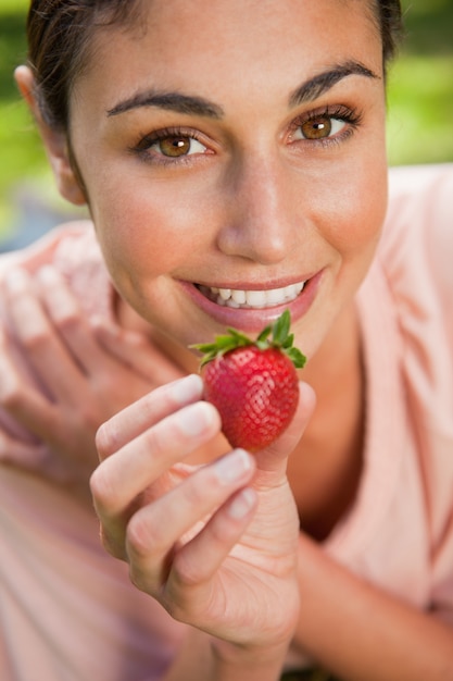 Woman offering a strawberry while lying in grass