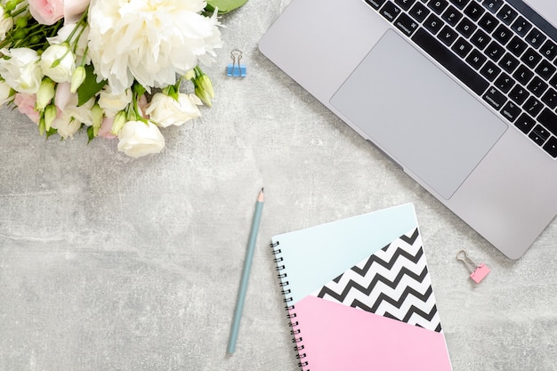 Woman office desk table with laptop computer, flowers, stylish diary notepad, stationery on concrete stone