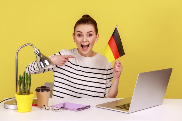 Woman office employee sitting at workplace and pointing at German flag job or education abroad