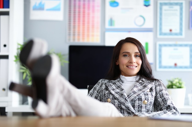 Woman in office put her feet on table and smiles.