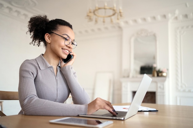 A woman in an office with glasses works uses a laptop answers the client's mail and phone