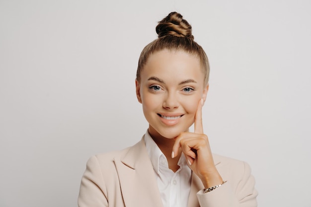 Woman office worker in beige suit hair in bun looking happily at camera confident gesture thinking of promotion posing on grey background