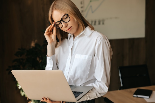 Woman office worker performs difficult tasks on a laptop, working on the internet in the office.