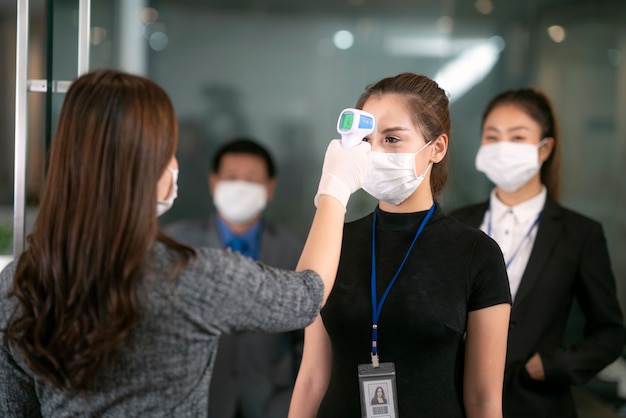 여성 장교 사용 스캐너 온도계는 작업을 위해 내부 사무실에 전달하기 전에 모든 사람의 온도를 확인합니다.