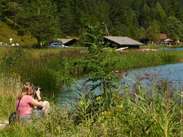 写真 湖の近くの草の上にいる女性が美しい景色を写真に撮ります