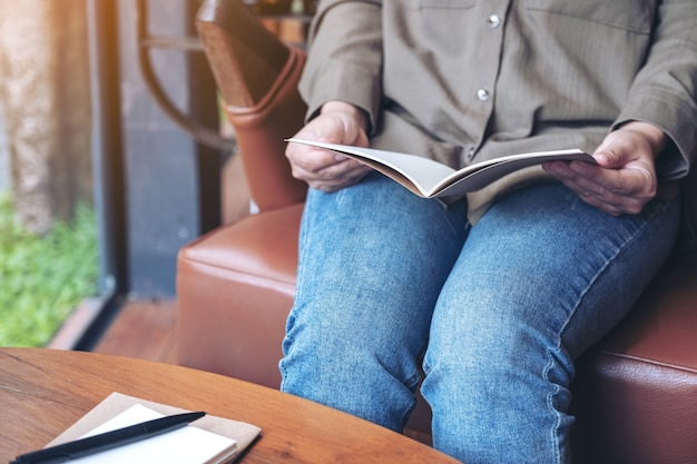 Donna che apre un libro da leggere con notebook e tazza di caffè sul tavolo di legno nella caffetteria