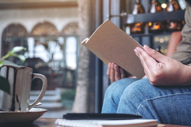 カフェの木製テーブルにノートとコーヒーカップで本を開く女性