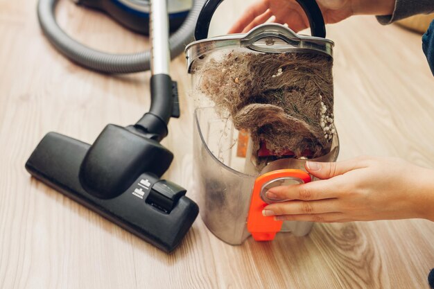 Woman opening dust filter of vacuum cleaner at home container full of dirt and cats hair