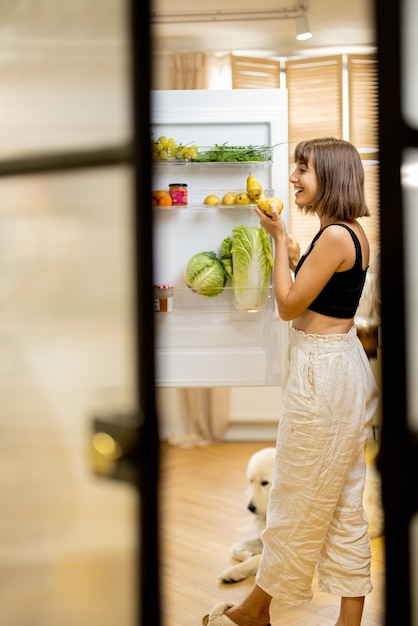 Foto la donna apre il frigorifero pieno di ingredienti alimentari sani