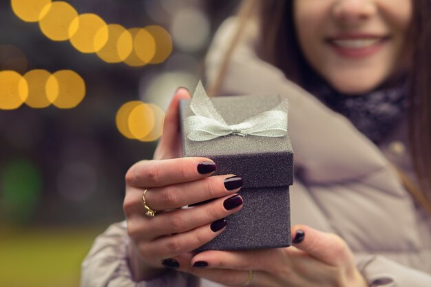 Photo woman opens a small gift box with a bow at the street with bokeh light