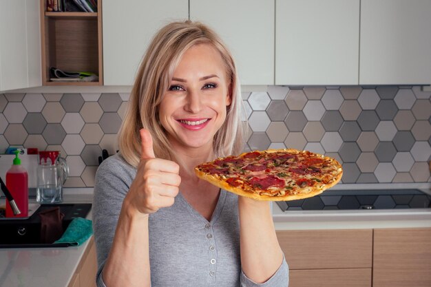 Donna che apre i forni e taglia la pizza con pomodori, olive, funghi e salsiccia al formaggio