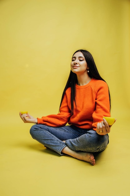 A woman in an orange sweater sits on a yellow background with the word lemon on her left hand.