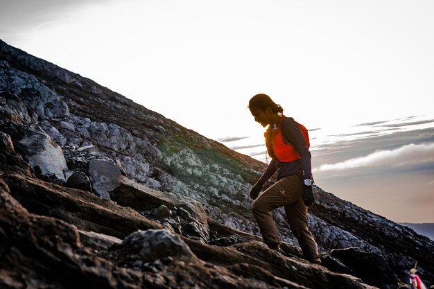 Photo a woman in an orange vest is climbing a rocky hill.