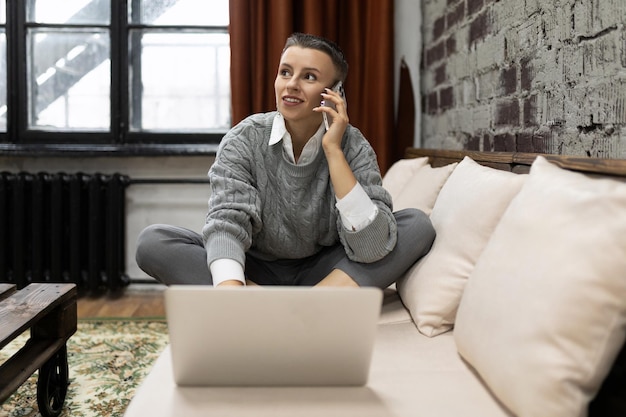 Woman ordering goods in the online store talking on the phone sitting on the sofa with a laptop