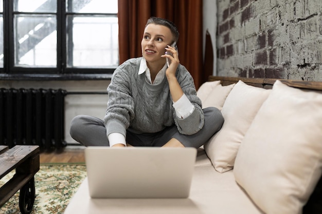 Woman ordering goods in the online store talking on the phone\
sitting on the sofa with a laptop