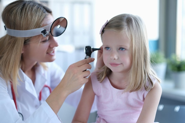 A woman otolaryngologist in a clinic looks at the ear of a girl