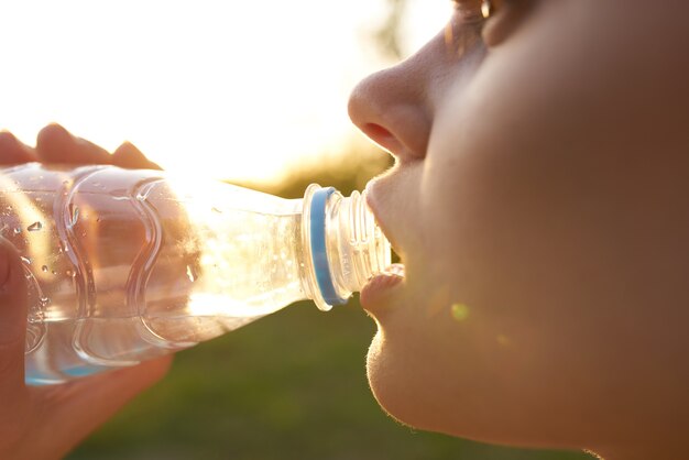 Woman outdoors drinking water from a bottle of refreshment