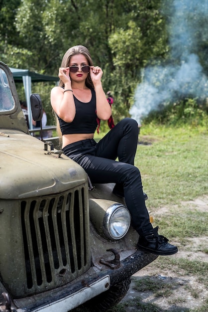 Woman outdoors sitting on hood of military car