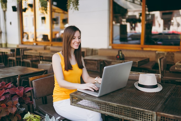 Woman in outdoors street coffee shop cafe sitting at table working on modern laptop pc computer, relaxing in restaurant during free time