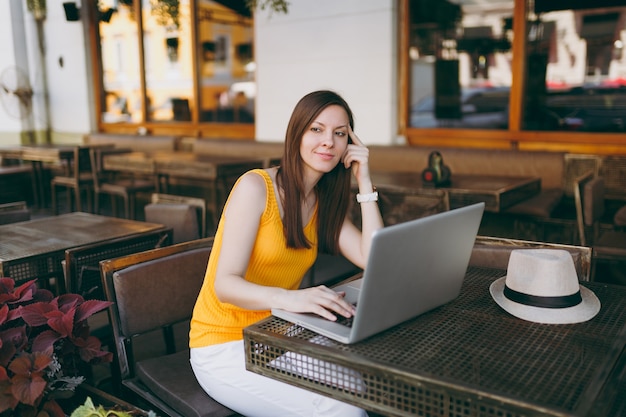 Woman in outdoors street coffee shop cafe sitting at table working on modern laptop pc computer, relaxing in restaurant during free time