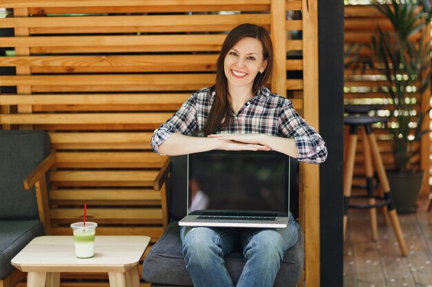 Woman in outdoors street coffee shop wooden cafe sitting in casual clothes, hold laptop pc computer with blank empty screen, relaxing in free time. Mobile Office