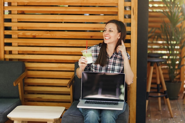 Woman in outdoors street coffee shop wooden cafe sitting in casual clothes, hold laptop pc computer with blank empty screen, relaxing in free time. Mobile Office