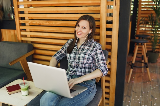 Woman in outdoors street summer coffee shop wooden cafe sitting in casual clothes, working on modern laptop pc computer