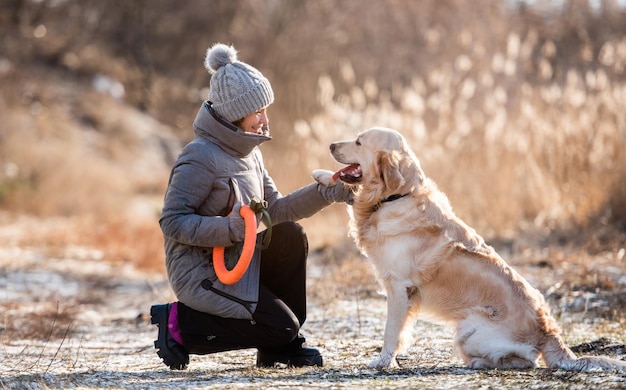 Woman owner holding paw of golden retriever dog during early spring walk outdoors and smiling lookin