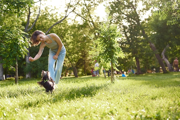 Foto proprietario della donna con il cane dell'yorkshire terrier che ha divertimento sull'erba. animale domestico del cane del cucciolo che funziona con le donne sul parco all'aperto