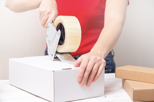 Foto scatole di cartone dell'imballaggio della donna facendo uso dell'erogatore del nastro