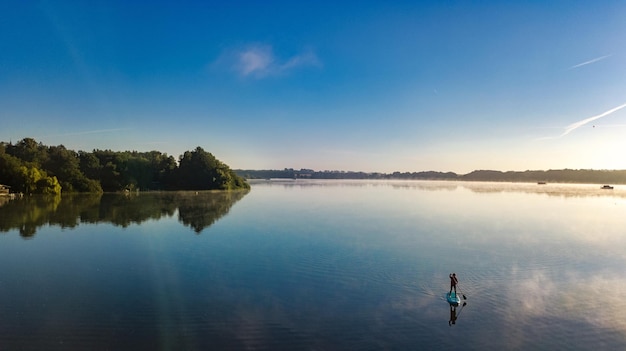 Donna che pagaia sulla tavola sup sul bellissimo lago durante il tramonto o l'alba in piedi sul paddle boarding