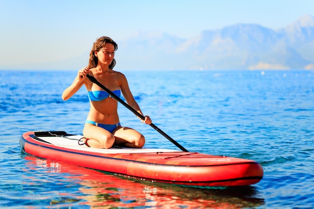 Donna che rema a bordo sup con le montagne sullo sfondo