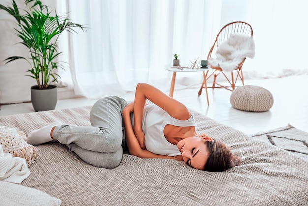 월경 기간 통증을 겪고 있는 손을 잡고 고통스러운 표정으로 침대에 누워 있는 여성